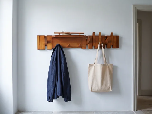 Illustrative wall-mounted wooden hanger with a navy coat and canvas bag